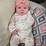 Adeline is registered to the contest to win money with this photo: baby, infant, child, onesie, headband, flower, blanket, patterned_blanket, cushion, blue_eyes, serious_expression, indoors, clothing, soft_toys, portrait, sitting, cute, comfortable, young_child, face