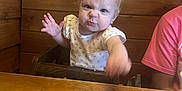 Layla joined the competition — help win amazing prizes! baby, toddler, child, wood, high_chair, table, plate, cup, person, face, expression, furniture, indoor, clothing, pink_shirt, light, hair, cute, funny_face, restaurant