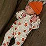 Layla is registered to the contest to win money with this photo: baby, newborn, sleeping, onesie, pumpkin_pattern, orange_hat, couch, blanket, infant, cozy, soft_fabric, indoors, cute, peaceful, resting, child, person, small_hands, footed_pajamas, autumn_theme