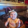 Layla is registered to the contest to win money with this photo: baby, child, high_chair, headband, smile, restaurant, table, wood, clothing, person, infant, seat, food, happy, cute, apparel, indoor, face, dining, furniture
