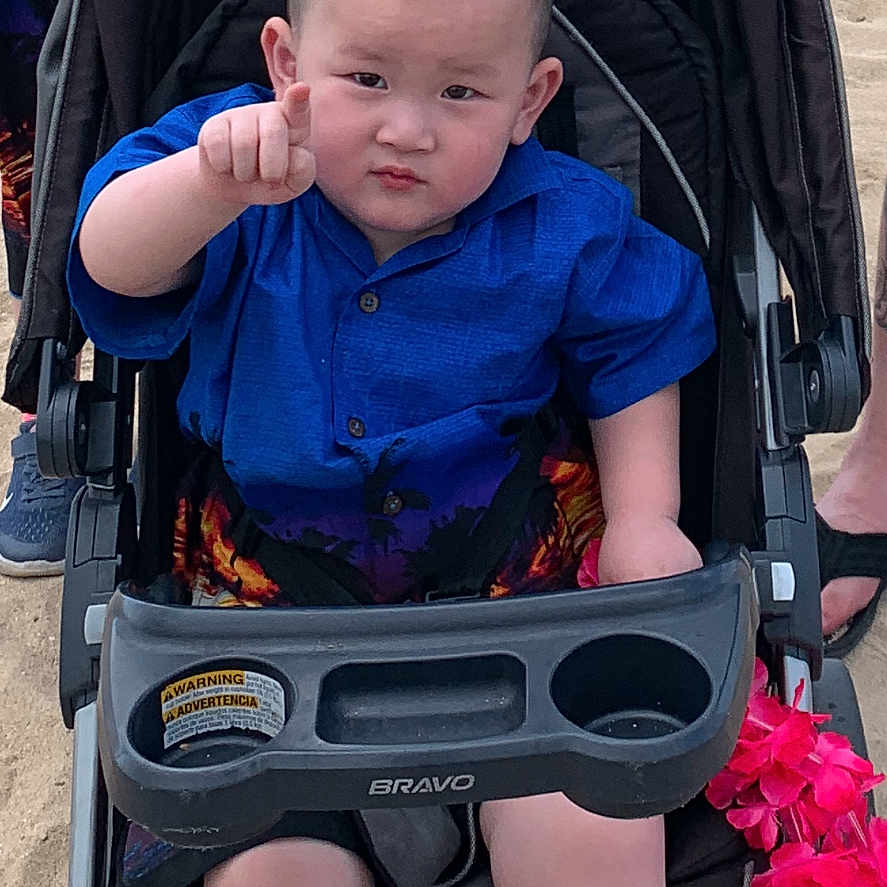 Jaydan Lau is registered to the contest to win money with this photo: beach, blue_shirt, casual, child, expression, family, footwear, hand, mohawk, outdoor, person, pointing, sand, shorts, stroller, summer, sunny, toddler, toy, vacation
