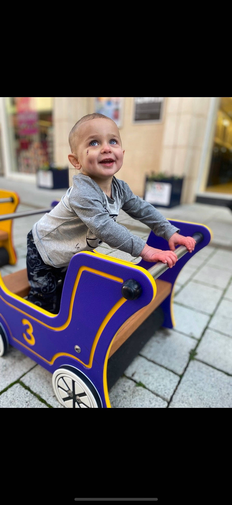 Kenston is registered to the contest to win money with this photo: automotive_design, baby, baby_toddler_clothing, child, comfort, electric_blue, fun, happy, joy, leisure, person, play, purple, recreation, riding_toy, room, sitting, smile, tire, toddler