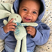 Kayden a rejoint le concours — aidez-le/la à gagner de superbes lots ! baby, child, hoodie, plush_bunny, toy, smile, happy, infant, blue_clothing, blanket, patterned_blanket, cute, portrait, face, hands, indoors, cozy, soft_toy, young_child, joyful