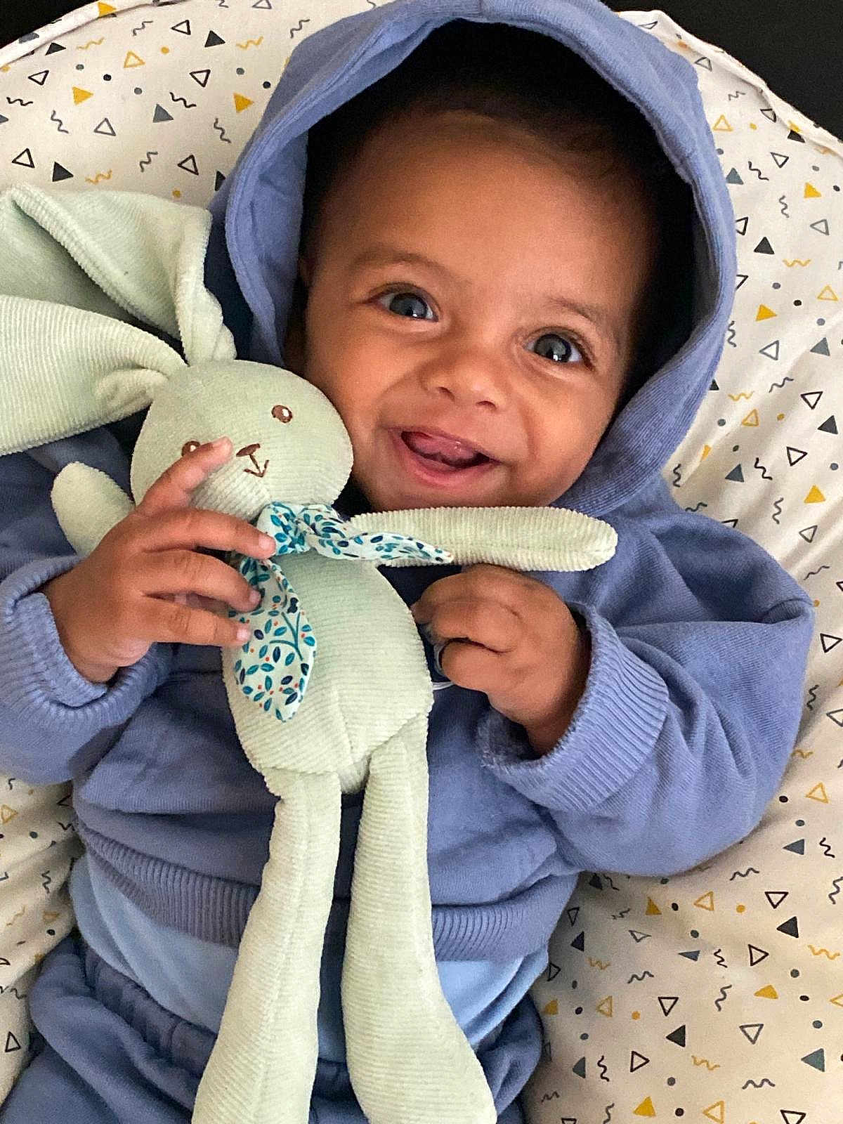 Kayden a rejoint le concours — aidez-le/la à gagner de superbes lots ! baby, child, hoodie, plush_bunny, toy, smile, happy, infant, blue_clothing, blanket, patterned_blanket, cute, portrait, face, hands, indoors, cozy, soft_toy, young_child, joyful