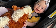 Lily is registered to the contest to win money with this photo: baby, car_seat, stuffed_animal, headband, smiling, blanket, infant, child, seatbelt, toy, happy, clothing, indoor, closeup, person, cute, soft_toy, car_interior, toddler, comfort