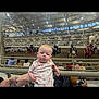 baby, infant, person, indoor, arena, horse, carriage, spectator, seating, railing, tattoo, event, crowd, light, ceiling, window, people, clothing, drink, hand