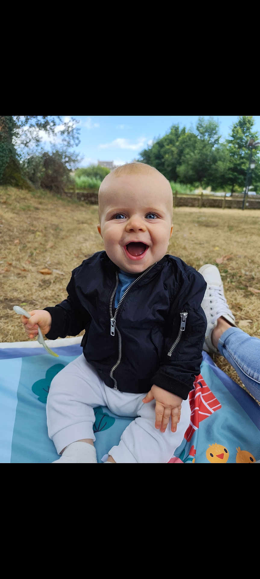 Liam participe au concours pour gagner de l'argent avec cette photo : baby, child, smiling, outdoor, grass, blanket, jacket, pants, fork, happy, person, blue_eyes, sitting, daylight, nature, trees, footwear, casual, park, joy