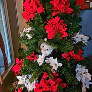 Eli joined the competition — help win amazing prizes! cat, christmas_tree, red_flowers, white_flowers, pine_cones, indoor, holiday_decor, greenery, curious_cat, peeking, festive, decorations, plant, pet, animal, fur, face, eyes, tree, nature