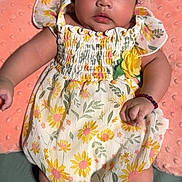 Madison is registered to the contest to win money with this photo: baby, child, infant, floral_dress, socks, bracelet, pillow, soft_texture, curly_hair, cute, portrait, indoors, lying_down, pink, yellow, green, white, skin, face, person