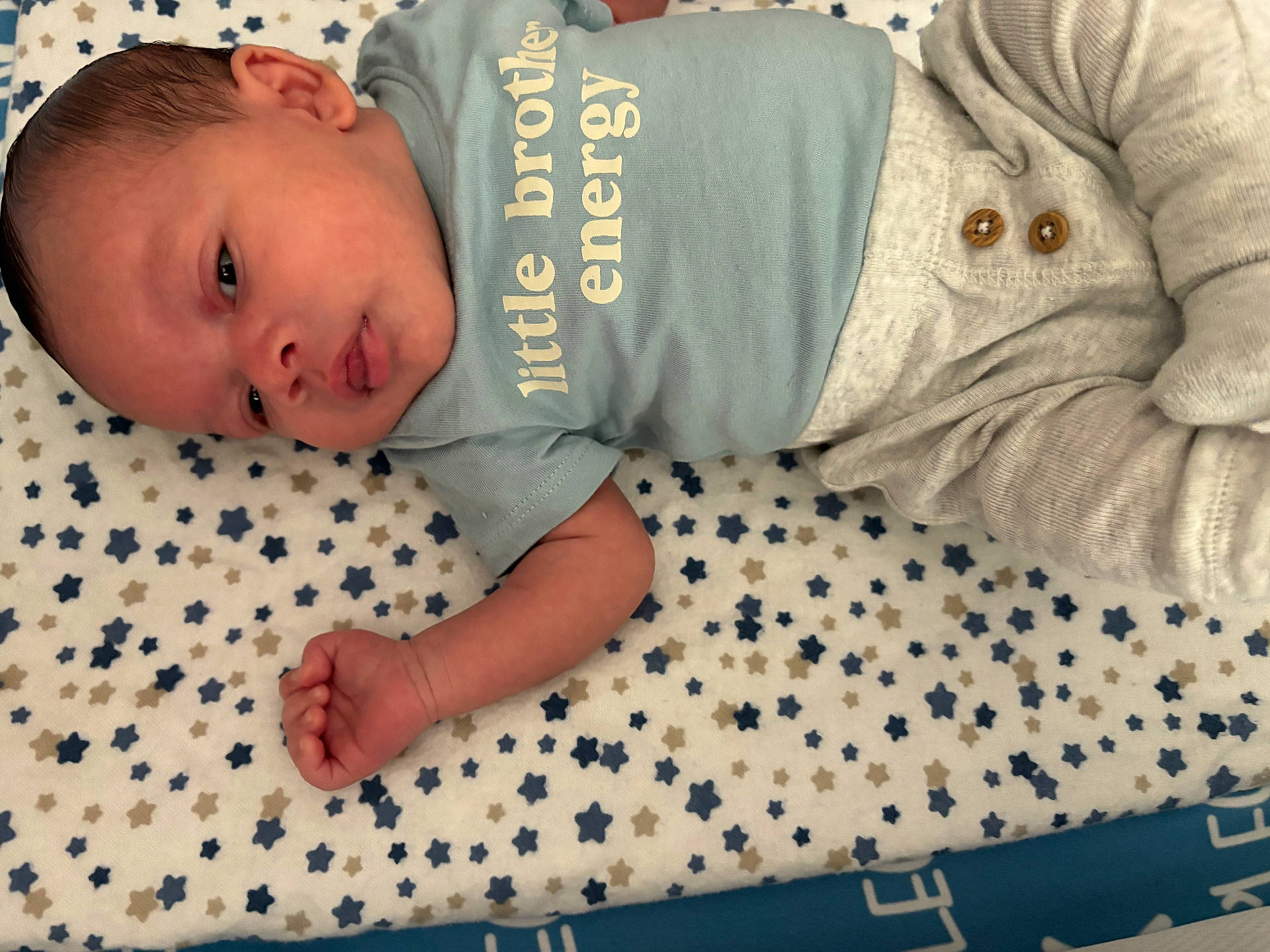 Alegend joined the competition — help win amazing prizes! baby, blanket, blue_shirt, child, cute, face, hand, human, indoors, infant, lying_down, newborn, pants, peaceful, portrait, skin, soft_fabric, star_pattern, text_on_clothing, wooden_buttons