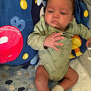 Alegend is registered to the contest to win money with this photo: baby, infant, child, dinosaur_onesie, green_clothing, socks, blanket, blue_blanket, patterned_blanket, cute, indoors, laying_down, face, expression, young_child, soft_toys, colorful, resting, small_hands, cozy