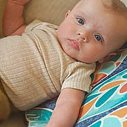 Enoch joined the competition — help win amazing prizes! baby, infant, child, portrait, lying_down, wide_eyed, blue_eyes, raised_hand, smiling, face, head, onesie, clothing, cushion, patterned_fabric, indoor, close_up, relaxed, photography, colorful_background
