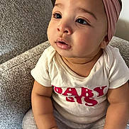 Solara joined the competition — help win amazing prizes! baby, baby_girl, barefoot, child, close_up, couch, curious, eyes, face, gray_pants, hands, headband, home, indoors, infant, pink_bow, portrait, sitting, soft_lighting, white_shirt