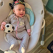 Vedanya Aruna Jain is registered to the contest to win money with this photo: baby, infant, smiling, onesie, headwrap, soccer_ball, baby_rocker, indoor, flooring, wood_floor, cozy, child, cute, pink, grey_clothing, toy, happy, playful, face, person