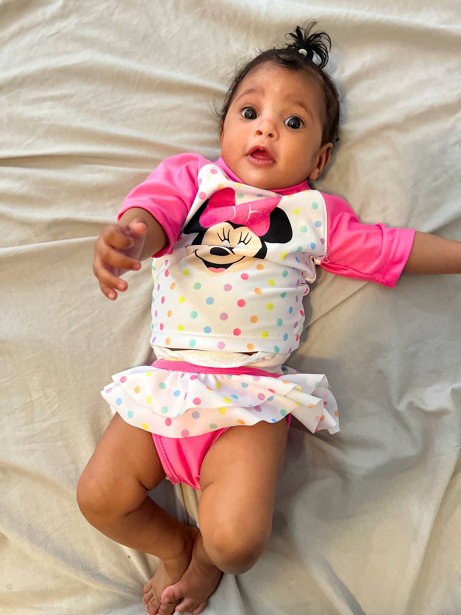 Amira is registered to the contest to win money with this photo: arm, baby, baby_toddler_clothing, comfort, day_dress, dress, eye, face, happy, head, human_body, leg, linens, lip, person, pink, skin, sleeve, surprise, textile