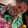 baby, infant, child, blanket, pink_blanket, green_blanket, toy, toys, floor, cute, smiling, playful, indoors, person, clothing, long_sleeve, patterned_clothing, face, head, bright_colors