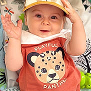 Rafaël a rejoint le concours — aidez-le/la à gagner de superbes lots ! baby, child, cap, hat, shirt, cartoon, animal_print, playful, smiling, raising_hand, cute, patterned_background, infant, clothing, face, portrait, happy, indoors, toy, toddler