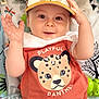 animal_print, baby, cap, cartoon, child, clothing, cute, face, happy, hat, indoors, infant, patterned_background, playful, portrait, raising_hand, shirt, smiling, toddler, toy