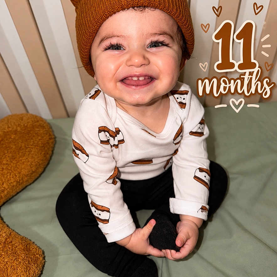 Hunter joined the competition — help win amazing prizes! baby, child, infant, smiling, happy, portrait, sitting, bed, bedroom, knit_hat, bear_hat, long_sleeves, black_pants, clothing, hands, face, teeth, striped_background, milestone, text_overlay