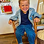 child, boy, smiling, wicker_chair, blue_jacket, jeans, blue_sneakers, indoor, wooden_floor, mirror, toys, shelf, happy, casual_clothing, portrait, furniture, room, young_child, seated, playful