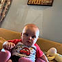 Jaxon is registered to the contest to win money with this photo: baby, child, infant, pink_baby_seat, cartoon_tshirt, living_room, curtains, stuffed_toy, couch, wall_art, decor, foot, face, person, seated, indoors, expression, clothing, home, comfort