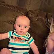 Jaxon is registered to the contest to win money with this photo: baby, infant, child, striped_clothing, couch, brown, seated, wide_eyes, curious, indoor, person, human, portrait, onesie, casual, expression, young, skin, hand, leg