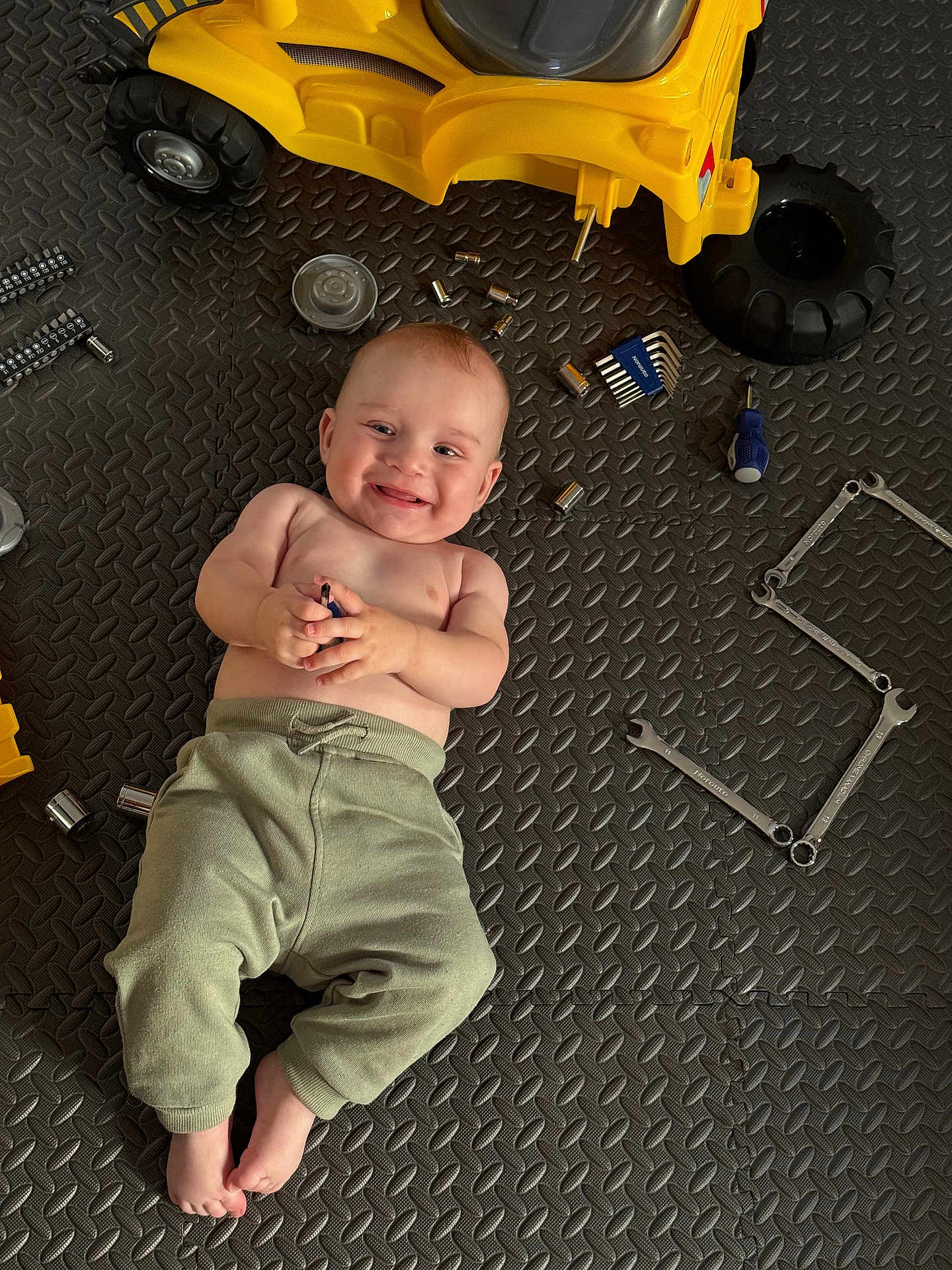 Yaroslav participe au concours pour gagner de l'argent avec cette photo : baby, child, smile, toy, yellow_toy, tools, wrenches, screwdriver, allen_keys, floor_mat, clothing, pants, bare_chest, foot, hand, face, playtime, indoor, happy, infant
