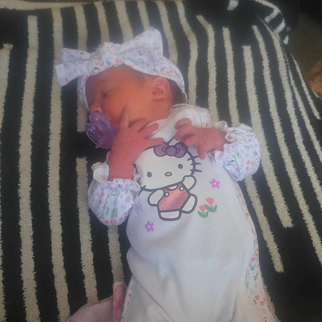 Joshlyn is registered to the contest to win money with this photo: baby, bag, blanket, bow_headband, clothing, cute, floor, hands, headband, hello_kitty, indoor, infant, legs, newborn, onesie, pacifier, portrait, sleeping, soft_lighting, striped_rug