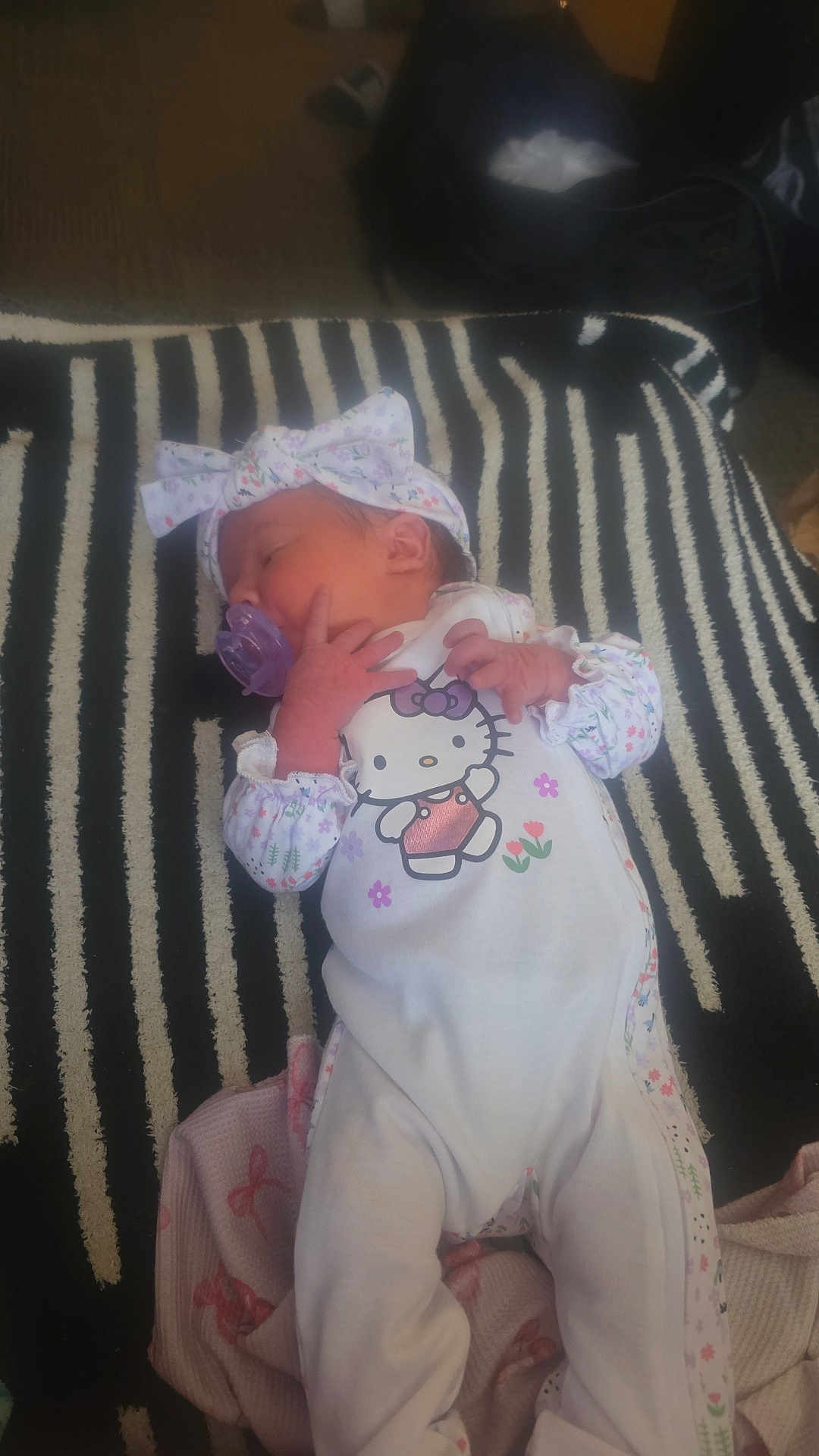 Joshlyn is registered to the contest to win money with this photo: baby, newborn, infant, pacifier, headband, bow_headband, hello_kitty, onesie, sleeping, striped_rug, blanket, legs, hands, indoor, portrait, cute, clothing, floor, bag, soft_lighting