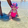 baby, child, swimsuit, sunhat, water, beach, tattoo, arm, sand, sea, summer, vacation, sunny, outdoor, people, colorful, sitting, shallow_water, portrait, curious