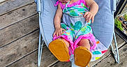 Star is registered to the contest to win money with this photo: baby, infant, child, sleeping, baby_rocker, hat, colorful_clothing, outdoor, wooden_deck, footwear, sun_hat, baby_seat, peaceful, toddler, cartoon_design, rainbow, monkey, relaxing, summer, cute