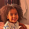 Jordan is registered to the contest to win money with this photo: child, smiling, afro_hair, bedroom, bed, dinosaur_print, tshirt, happy, indoor, person, portrait, curly_hair, young_child, clothing, furniture, towel, cabinet, skin, face, seated