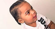 Jordan joined the competition — help win amazing prizes! child, braided_hair, white_shirt, text_on_clothing, curious_expression, portrait, indoor, light_background, young_child, person, casual_clothing, short_sleeves, skin, face, head, seated, looking_sideways, bracelet, cute, closeup