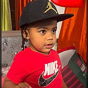 Jordan is registered to the contest to win money with this photo: child, toddler, cap, nike_shirt, red_clothing, indoor, curtains, heart_emoji, braids, earrings, social_media_screenshot, phone_screen, person, portrait, cute, young_child, expression, colorful_background, hand, standing