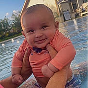 Valentino is registered to the contest to win money with this photo: baby, child, smiling, pool, water, swimming, outdoor, sunset, person, holding, happy, summer, toddler, swim_shirt, face, arms, skin, palm_tree, house, recreation