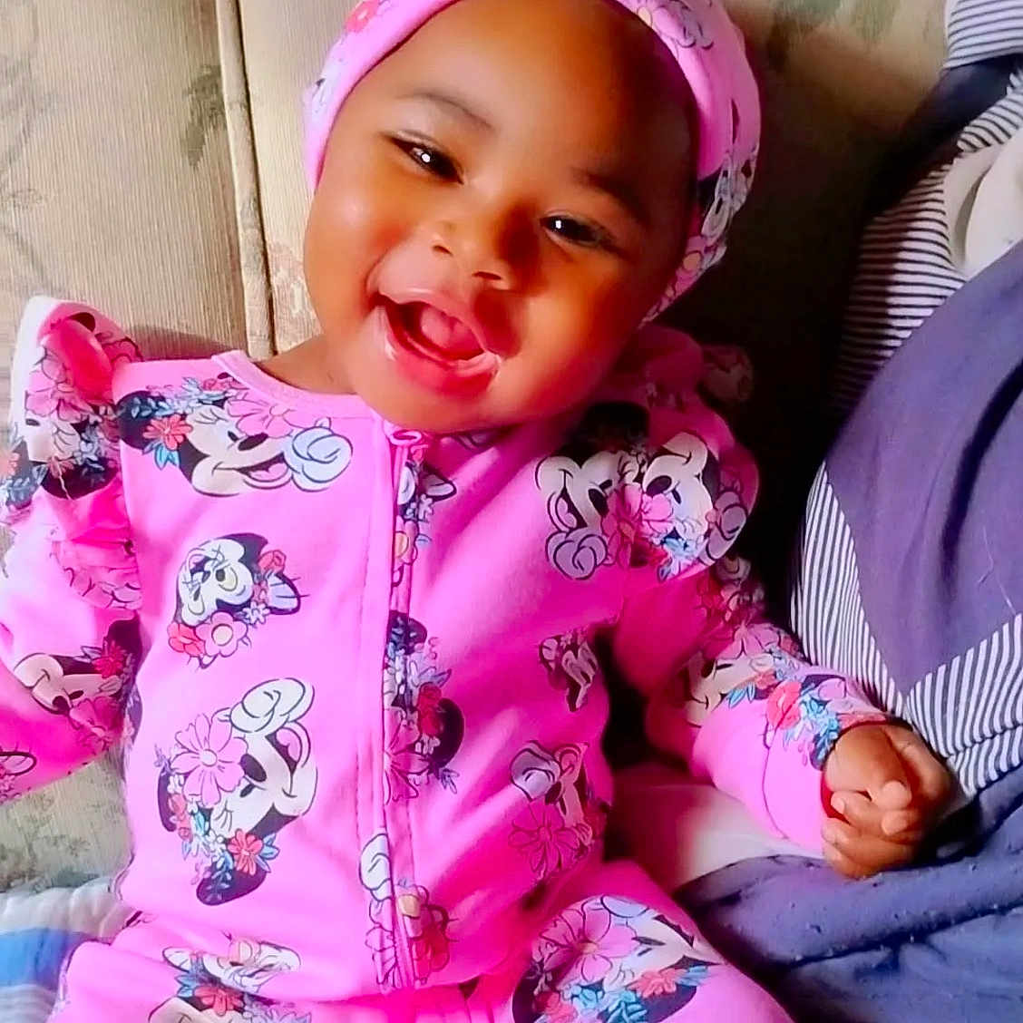 E'Mani is registered to the contest to win money with this photo: toddler, child, smiling, pink_clothing, minnie_mouse, headwear, sitting, couch, floral_pattern, happy, indoors, portrait, baby, cute, young_child, cozy, bright_colors, playful, fashion, person