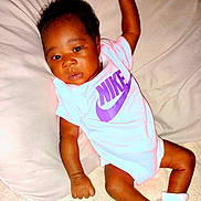 E'Mani is registered to the contest to win money with this photo: baby, infant, child, nike, onesie, booties, clothing, cute, lying_down, soft_surface, indoors, skin, face, hand, footwear, portrait, young_child, relaxed, pillow, curious