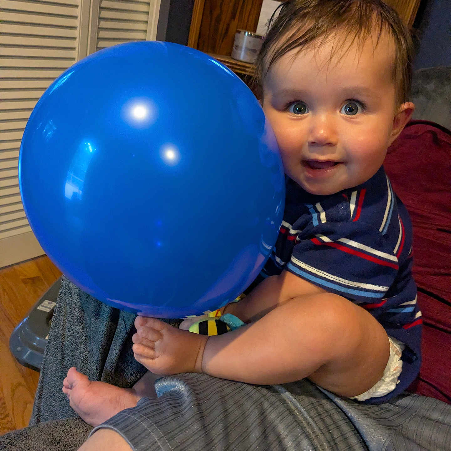 Nolan joined the competition — help win amazing prizes! baby, balloon, blue_balloon, child, indoor, striped_shirt, smiling, happy, person, face, foot, hand, seated, wooden_furniture, cushion, home, diaper, cute, portrait, toddler