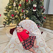Faith is registered to the contest to win money with this photo: baby, infant, christmas_tree, holiday_decor, plaid_skirt, red_top, blanket, headband, indoor, floor_tiles, ornaments, lights, festive, cute, child, person, holiday, seated, decorations, home