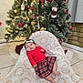 baby, infant, christmas_tree, holiday_decor, plaid_skirt, red_top, blanket, headband, indoor, floor_tiles, ornaments, lights, festive, cute, child, person, holiday, seated, decorations, home