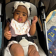 Danielle is registered to the contest to win money with this photo: baby, child, stroller, headband, bib, indoor, carpet, cute, pouting, legs, socks, clothing, seatbelt, curly_hair, infant, person, portrait, expression, cozy, baby_toy