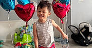 Ignacio is registered to the contest to win money with this photo: balloons, barefoot, blue_balloons, car_seat, child, colorful, dinosaur_toy, door, floor, happy, heart_shaped_balloons, home, indoor, living_room, painting, pajamas, person, playful, smiling, toys