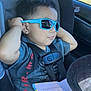 toddler, child, sunglasses, car_seat, seatbelt, book, hat, blue, shirt, jeans, window, car_interior, person, young_child, relaxed, sunlight, hands, cool, portrait, casual