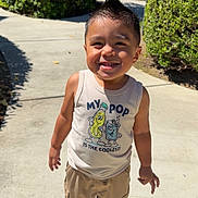 James is registered to the contest to win money with this photo: child, toddler, smiling, outdoor, sidewalk, greenery, bushes, sunlight, shorts, tank_top, sandals, happy, hair, spiky_hair, casual_clothing, residential_area, daylight, person, portrait, cute