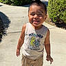 child, toddler, smiling, outdoor, sidewalk, greenery, bushes, sunlight, shorts, tank_top, sandals, happy, hair, spiky_hair, casual_clothing, residential_area, daylight, person, portrait, cute