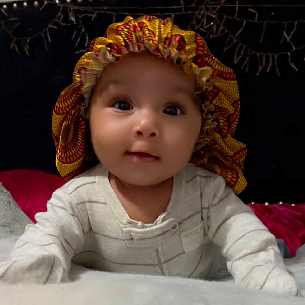 Leilani is registered to the contest to win money with this photo: baby, bonnet, cap, clothing, crawling, face, happy, hat, head, person, sitting, sunhat