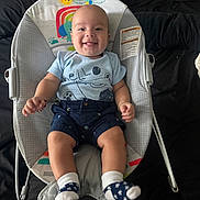 íker joined the competition — help win amazing prizes! baby, smiling, baby_rocker, blue_shirt, navy_shorts, socks, indoor, child, happy, infant, seat, fabric, toy_pattern, cute, person, clothing, footwear, sitting, face, portrait