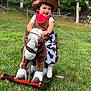 toddler, child, cowboy, rocking_horse, plush_toy, hat, bandana, outdoor, grass, greenery, costume, smiling, happy, play, toy, nature, daylight, cute, fun, portrait