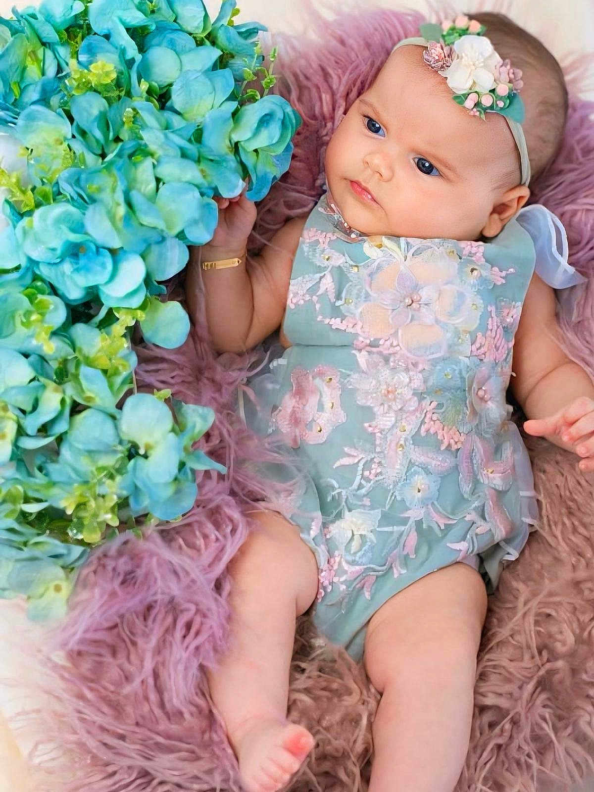 Ilanne a rejoint le concours — aidez-le/la à gagner de superbes lots ! baby, infant, flower, blue_flower, floral_dress, headband, blanket, soft_texture, cute, child, portrait, skin, hand, foot, laying_down, indoors, pastel_colors, decorative, adorable, young