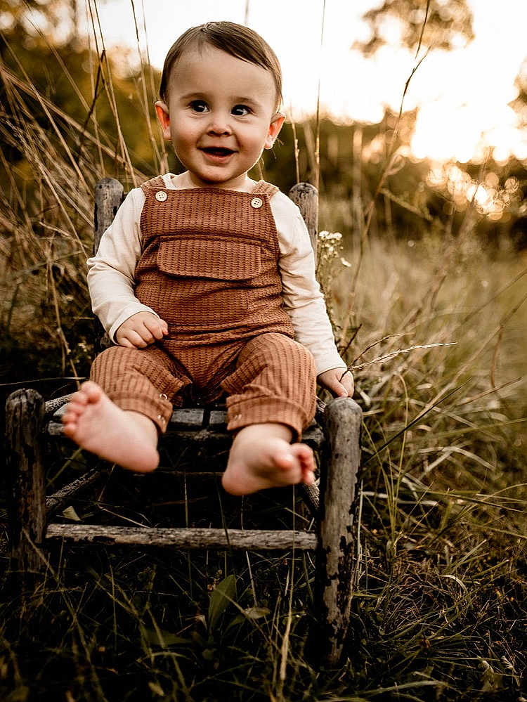 Cody joined the competition — help win amazing prizes! toddler, child, smiling, barefoot, overalls, long_sleeve_shirt, wooden_chair, outdoor, grass, nature, sunset, golden_hour, portrait, happy, young_child, rustic, field, cute, sitting, innocence